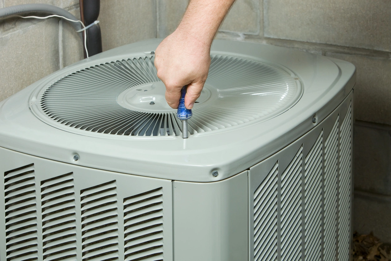 A hand using a screwdriver to open an outdoor air conditioning unit. 