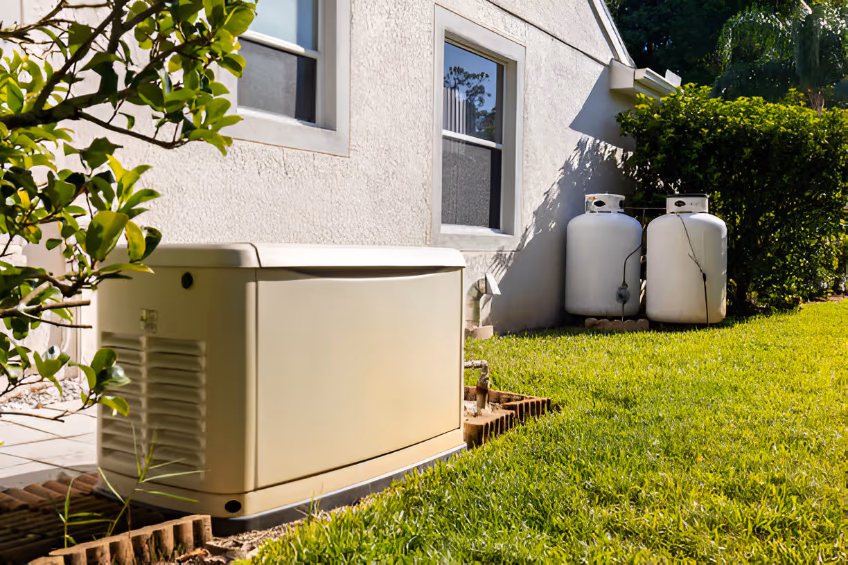 Home backup generator and propane tanks on green lawn beside white house
