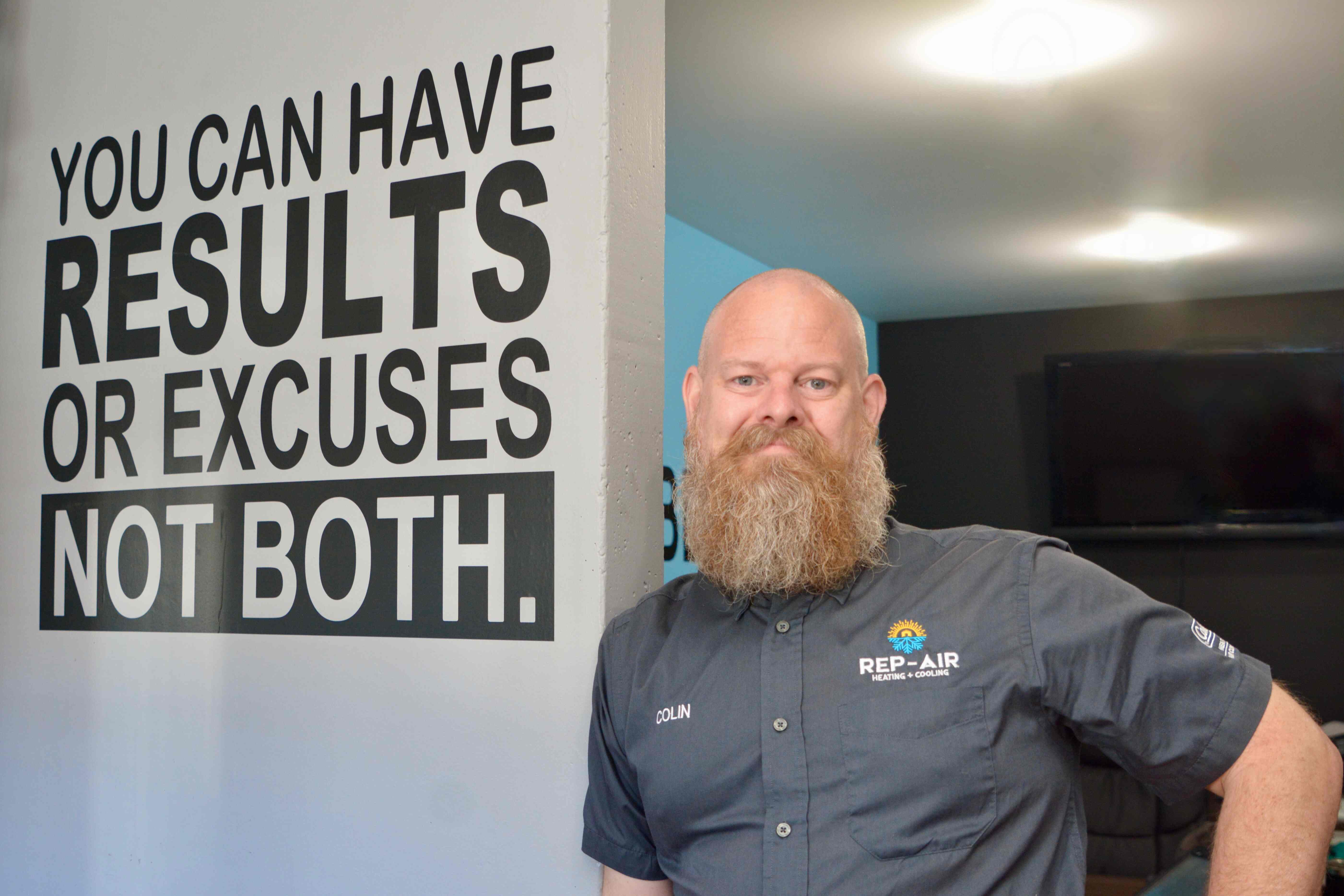 Bearded worker standing next to motivational sign about results and excuses
