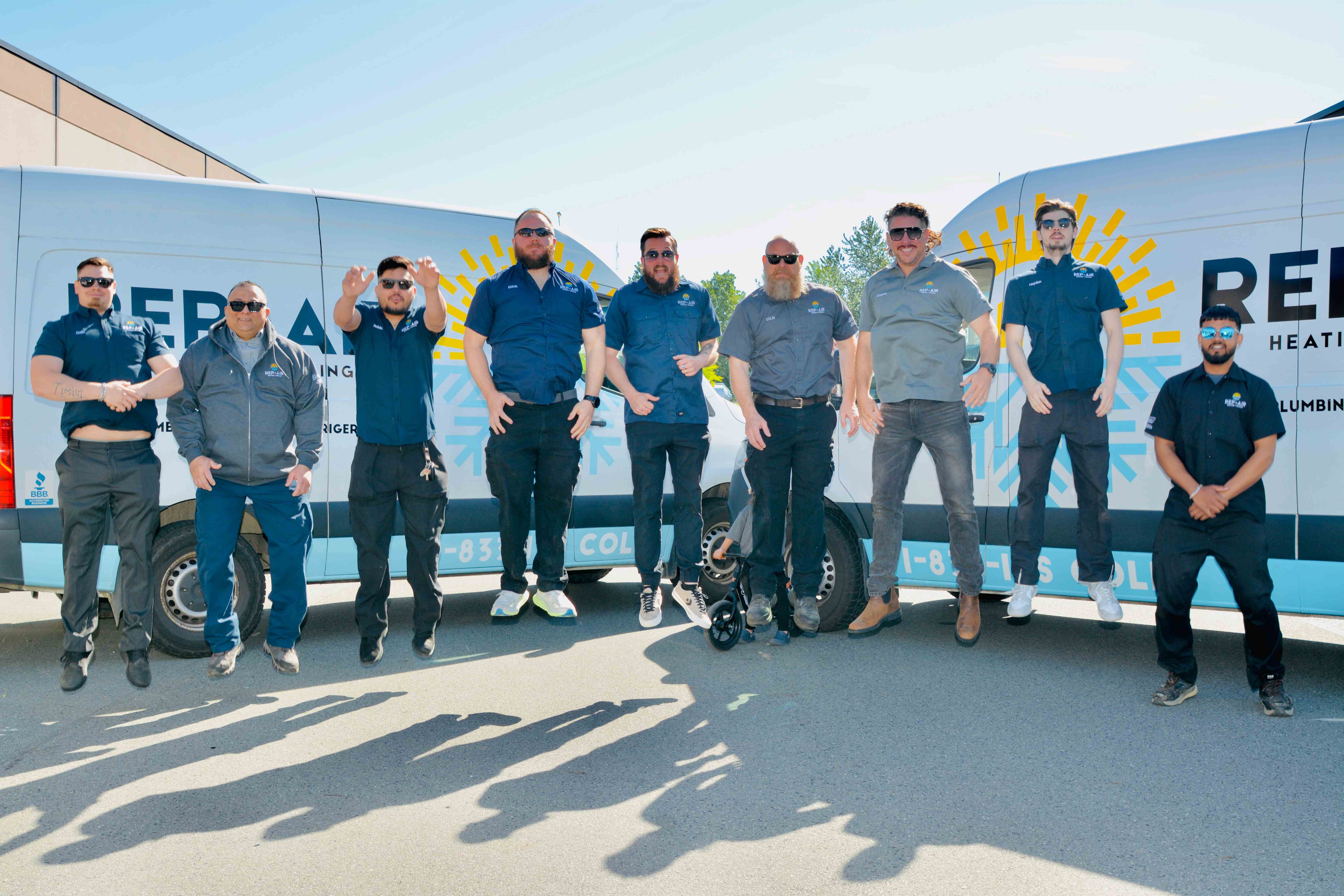Team of technicians posing together in front of service vehicles