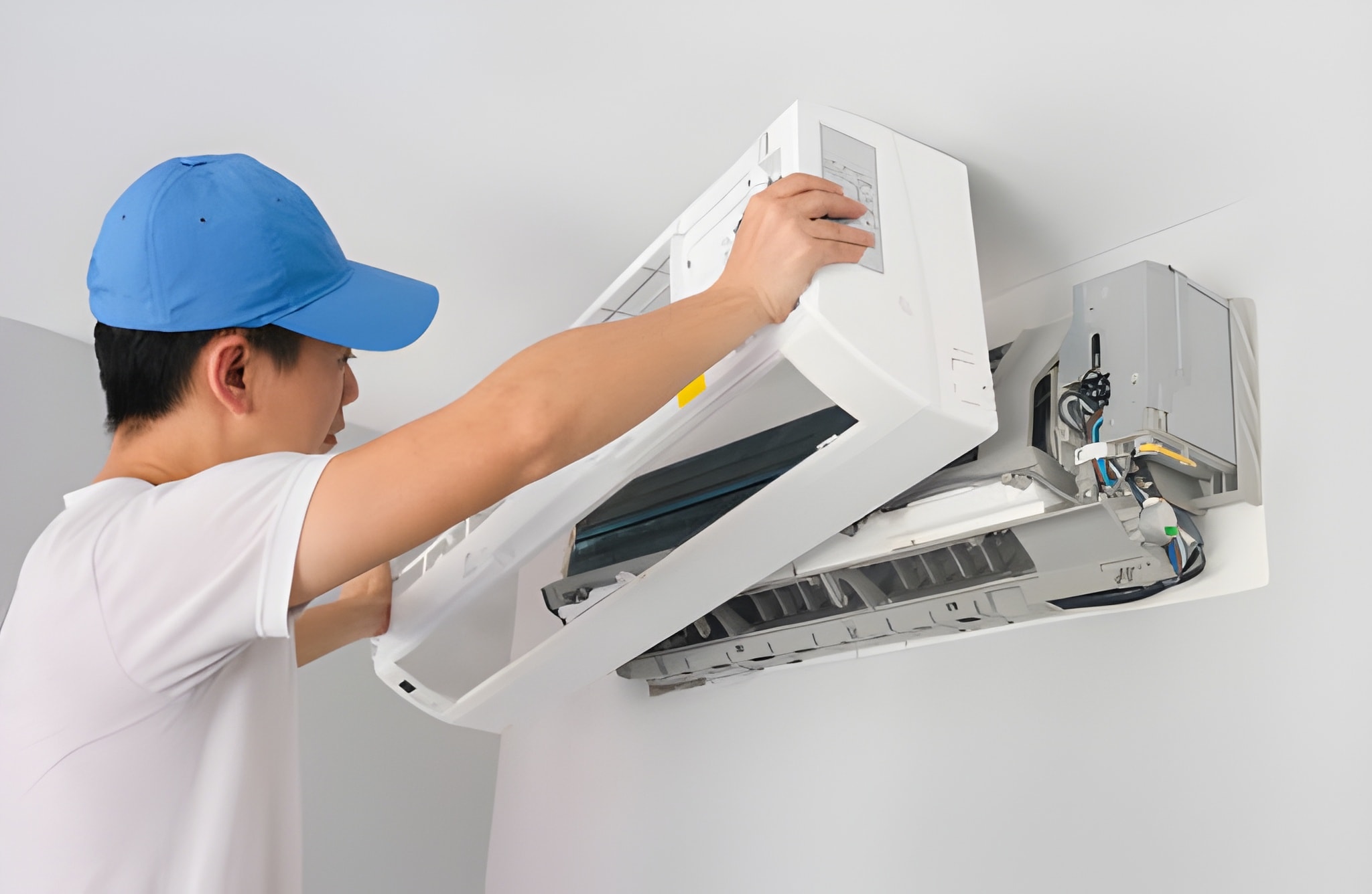 Technician in blue cap installing or repairing a wall-mounted air conditioner