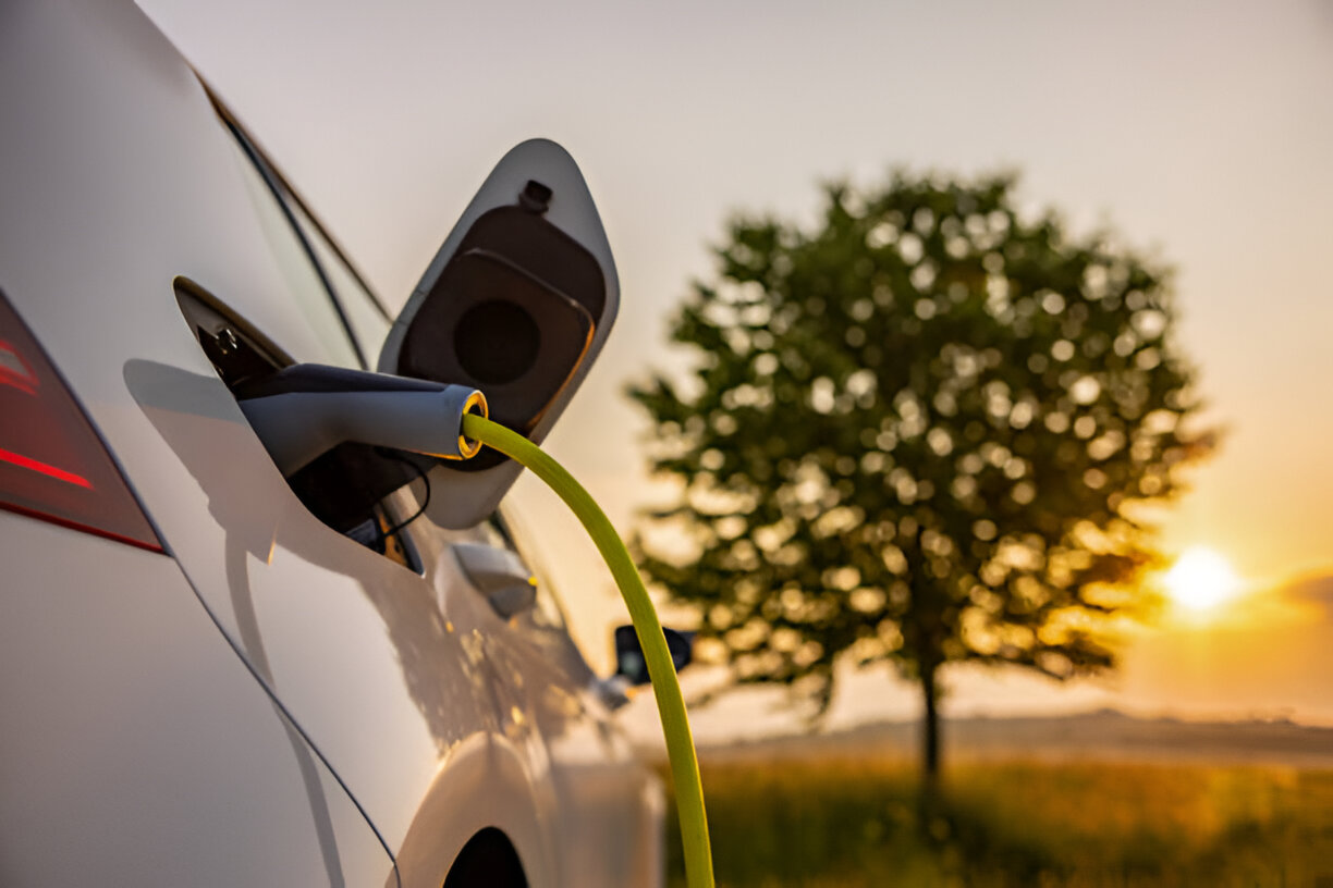 Electric car charging at sunset with tree in background, symbolizing green energy