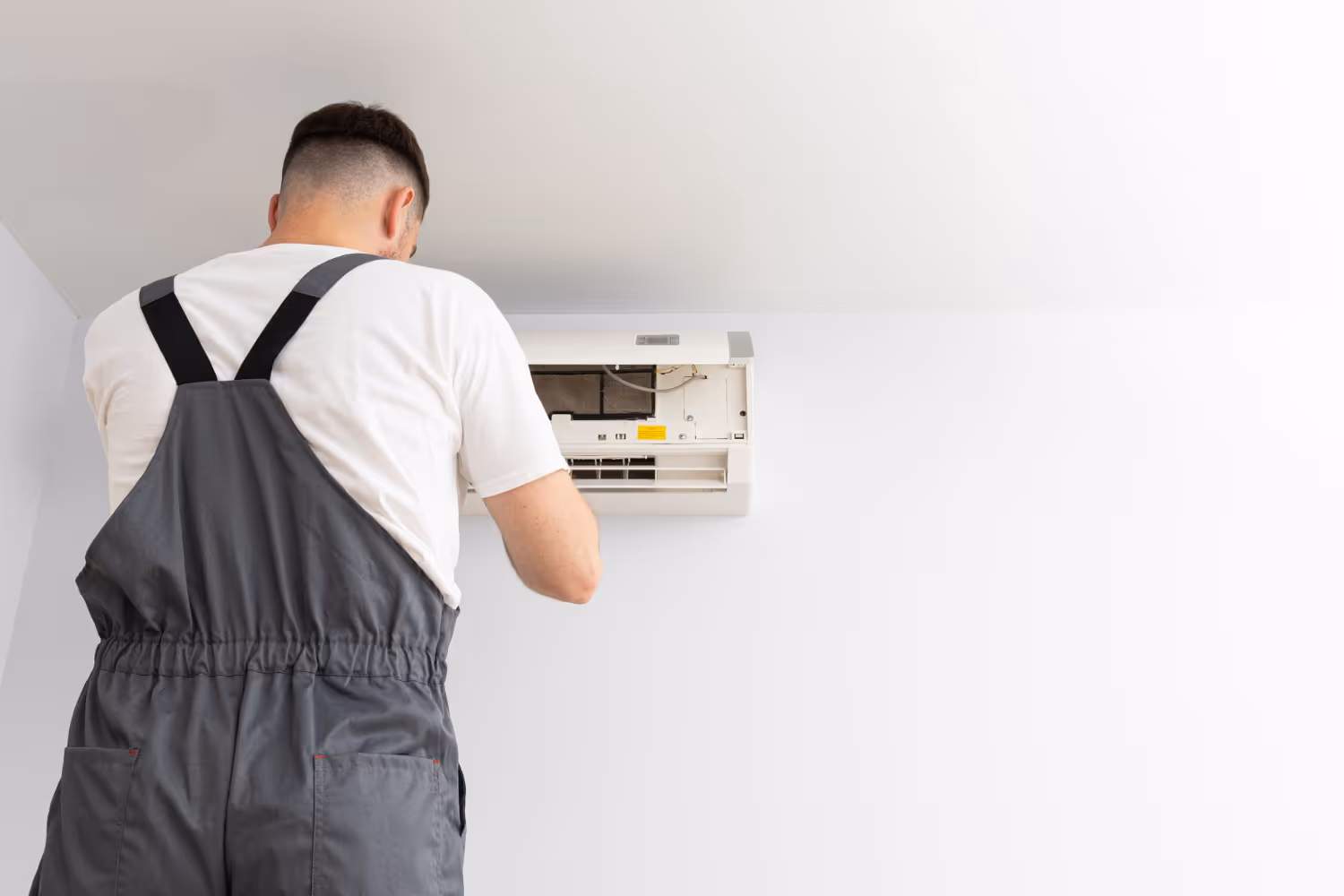 Technician in gray overalls fixing wall-mounted air conditioning unit
