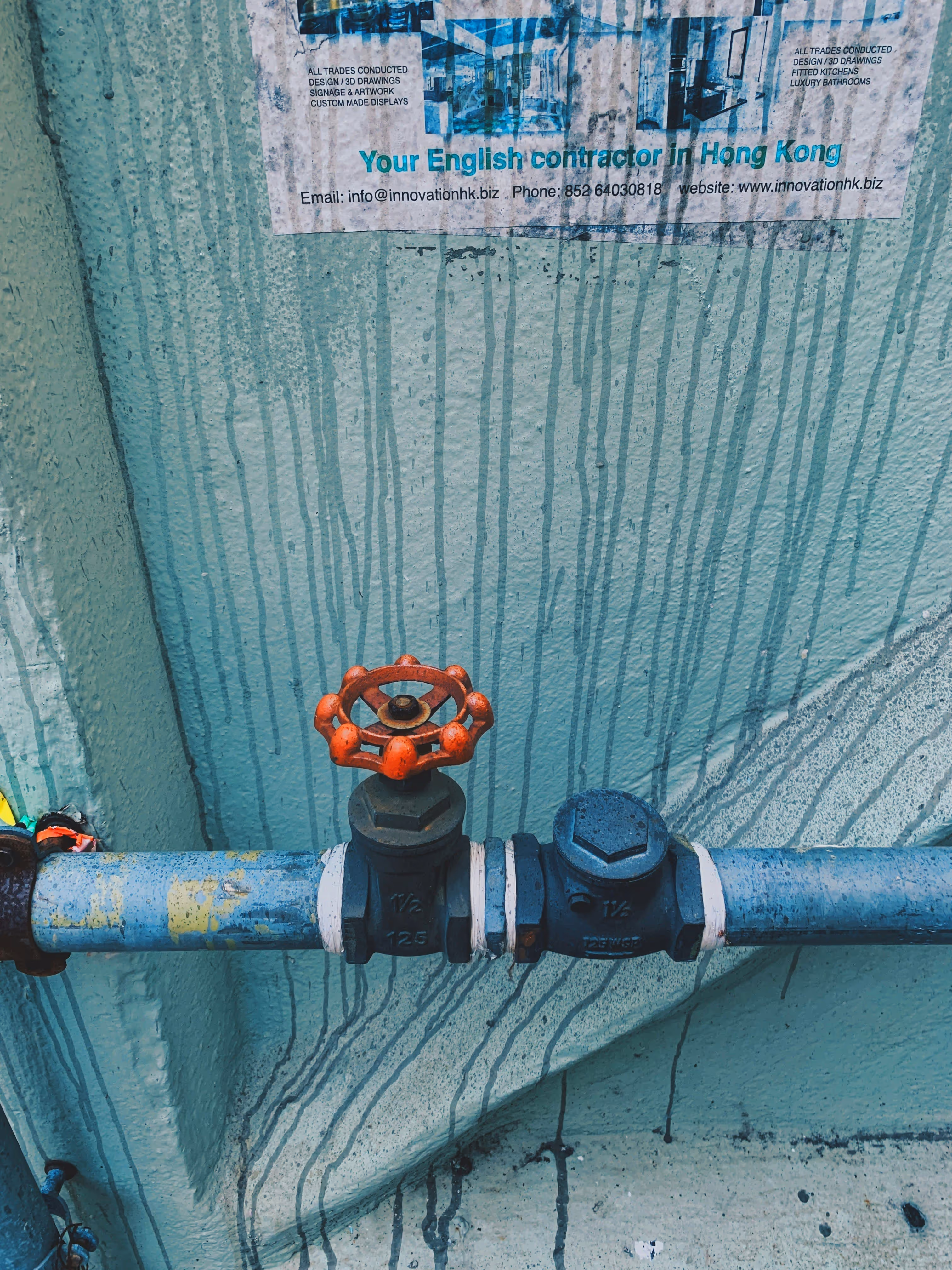 Red valve on blue pipe with Hong Kong contractor advertisement in background