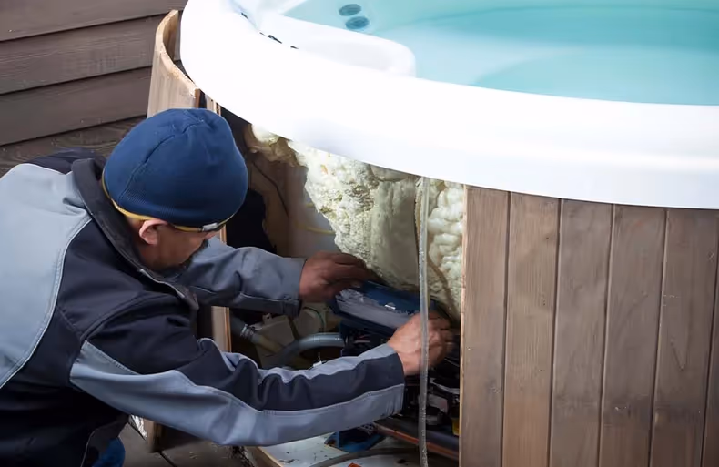 Technician in blue cap repairing hot tub equipment underneath wooden paneling