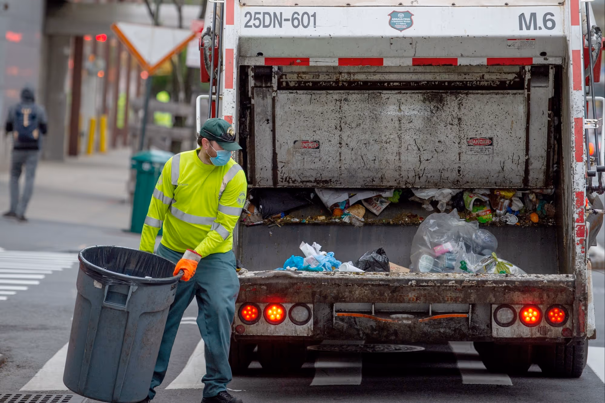 Garbage collector in high-visibility vest loading trash into municipal truck