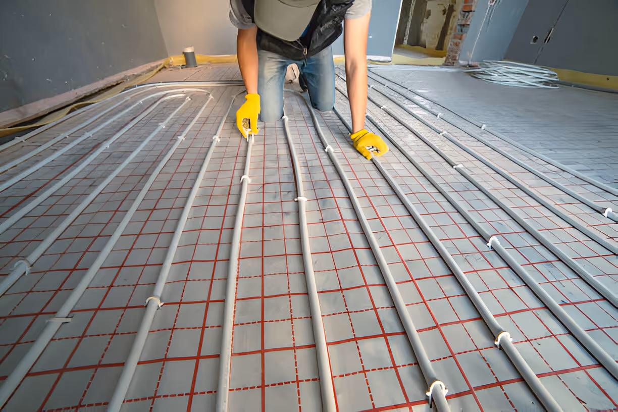 Installer laying radiant floor heating pipes on red mesh grid