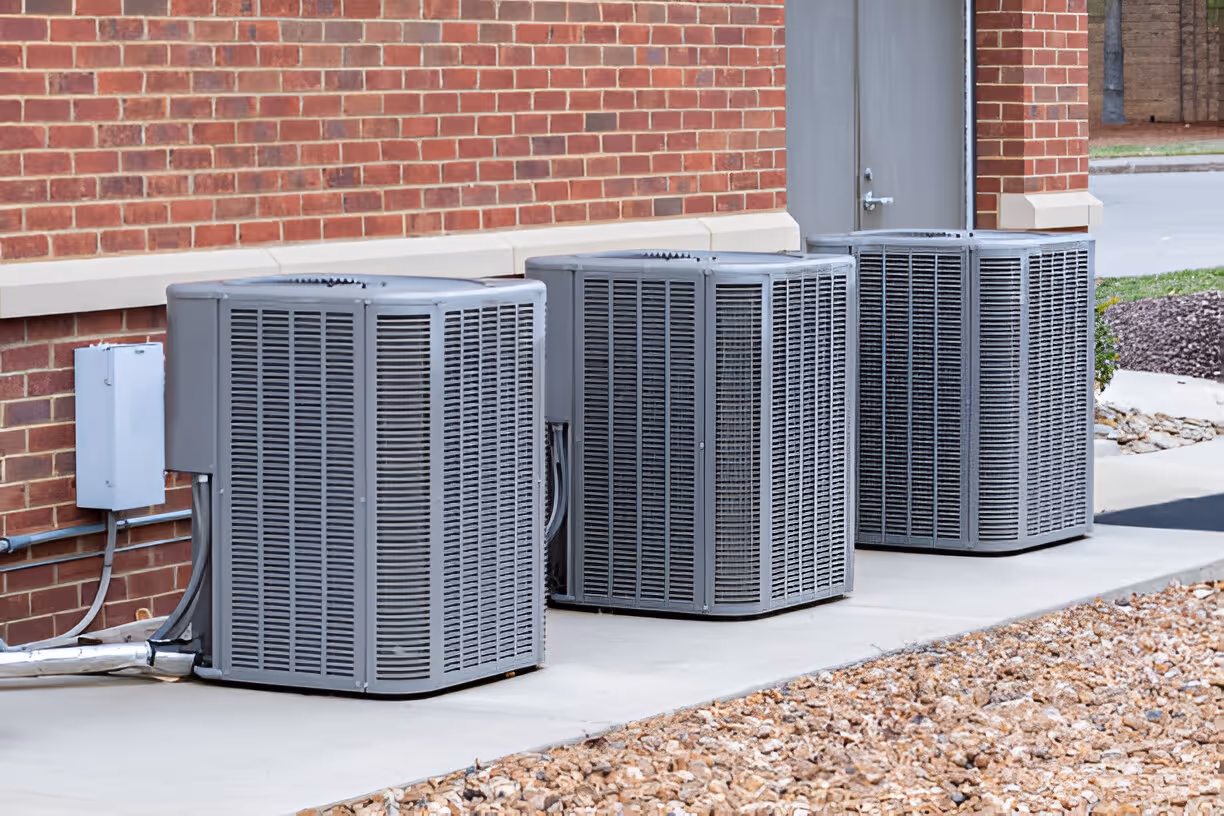Multiple air conditioning units lined up against a brick wall exterior