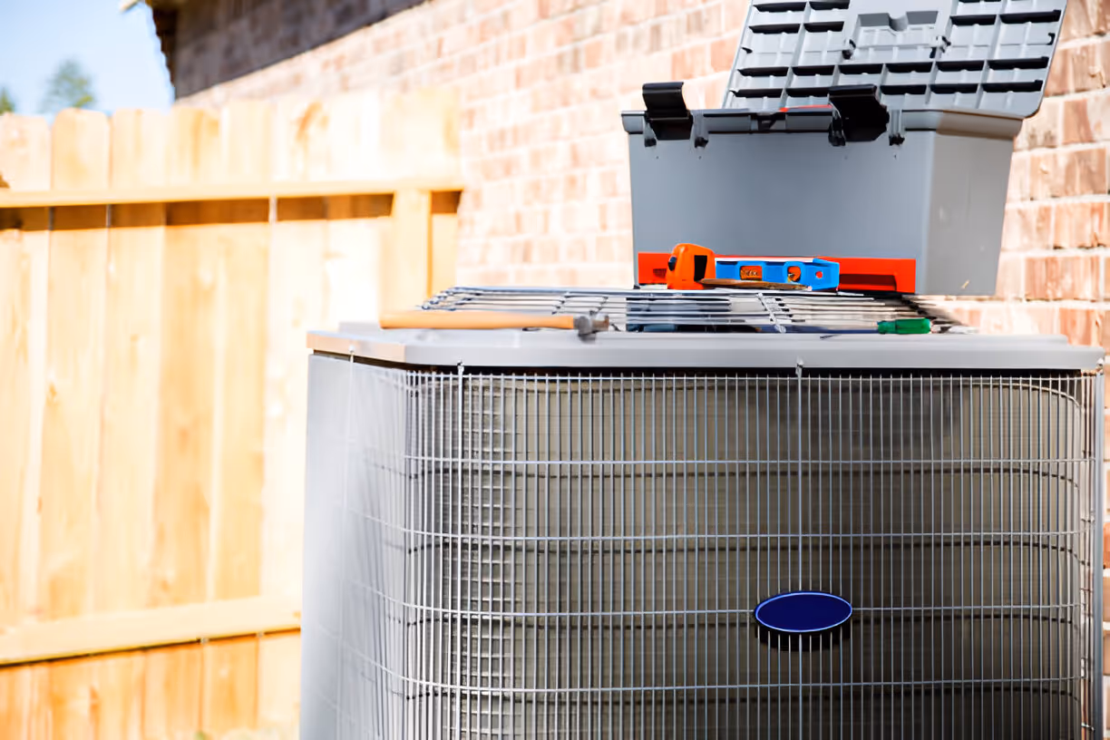 Air conditioning unit with tools on top, situated near wooden fence