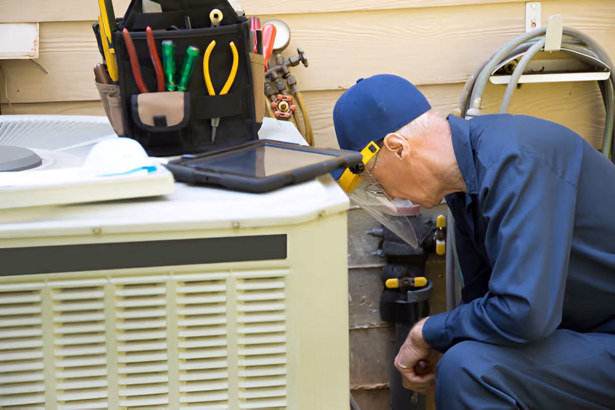 Technician in blue uniform inspecting equipment with tool bag nearby