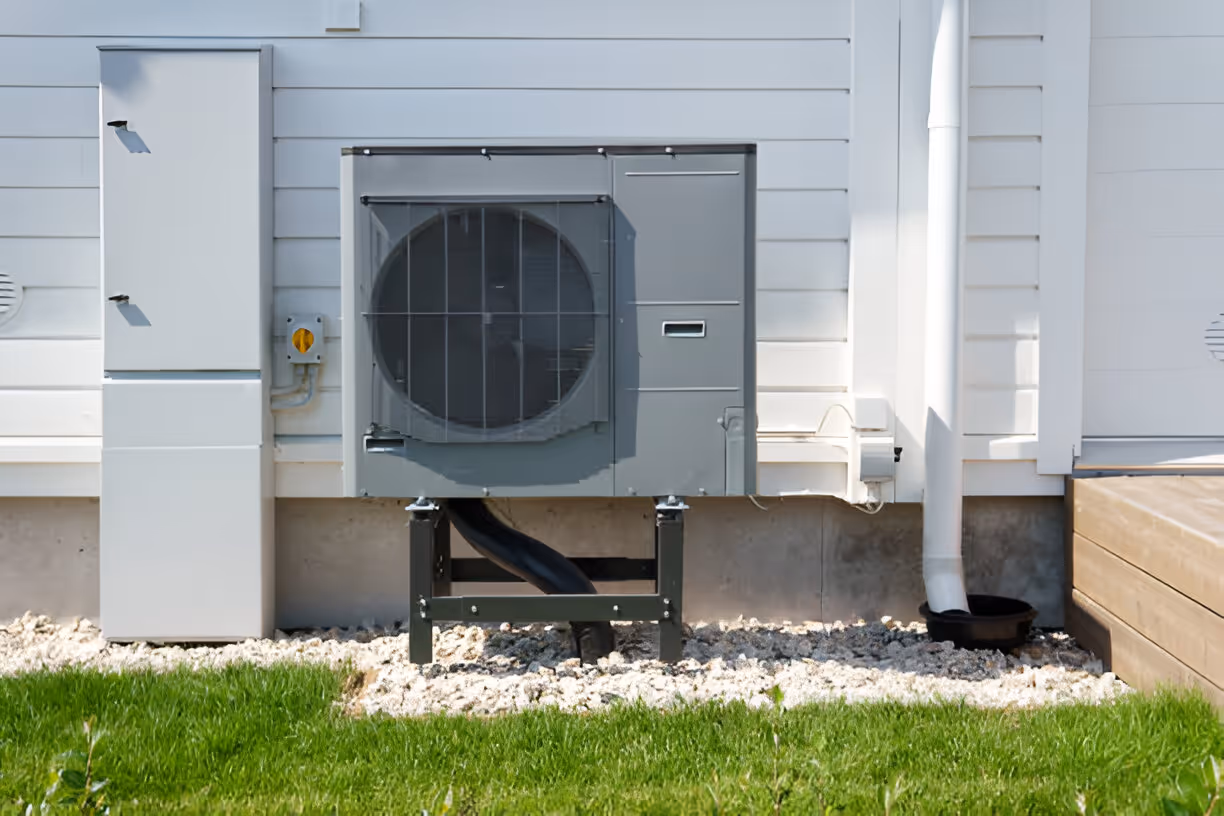 Gray heat pump installed on concrete base beside white building and green grass