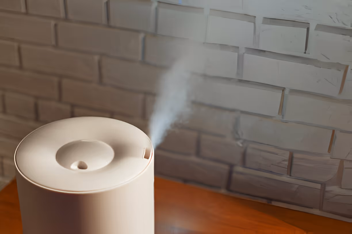 White air humidifier emitting steam against brick wall background