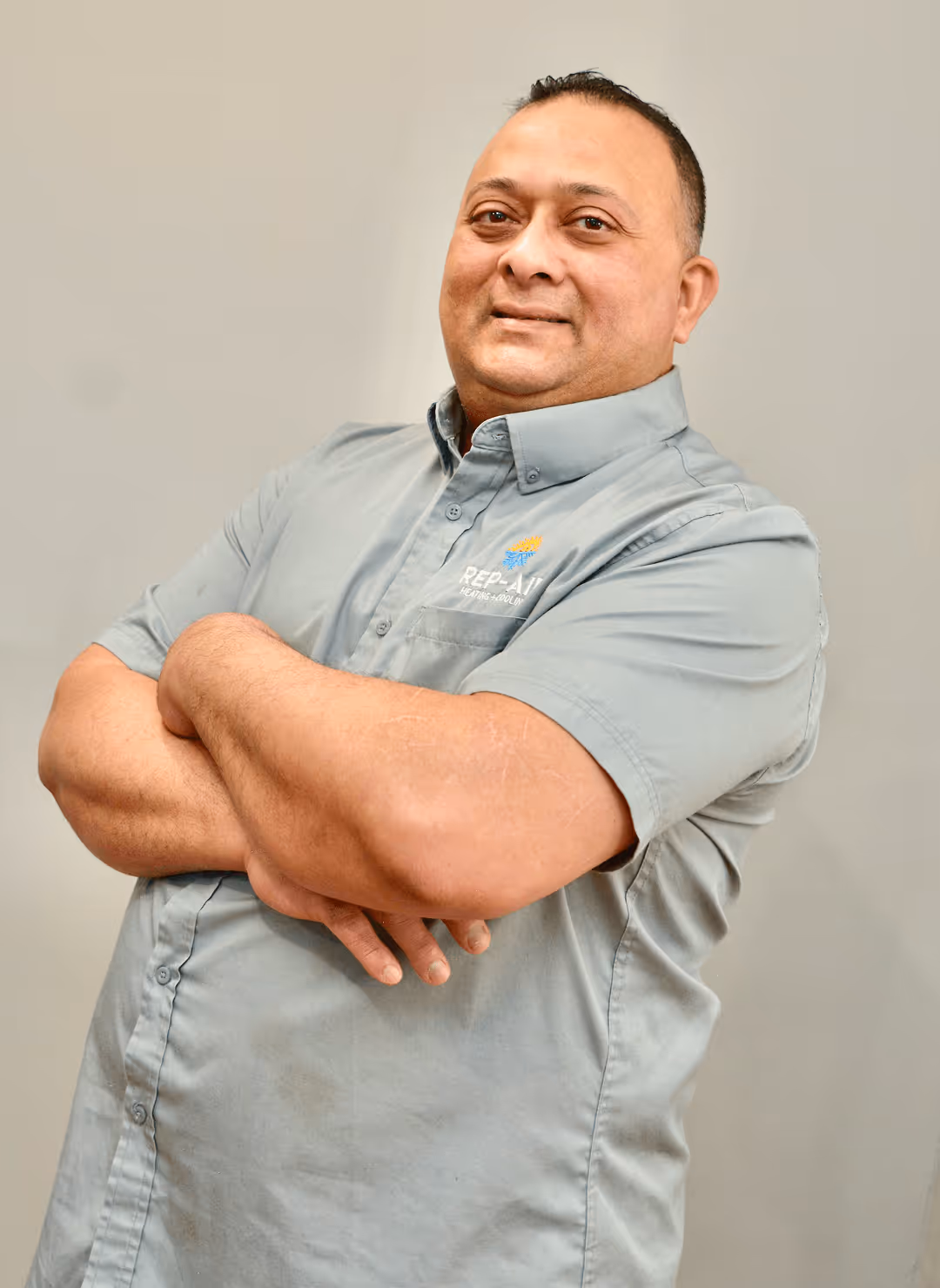 Smiling employee in gray shirt with crossed arms looking confident