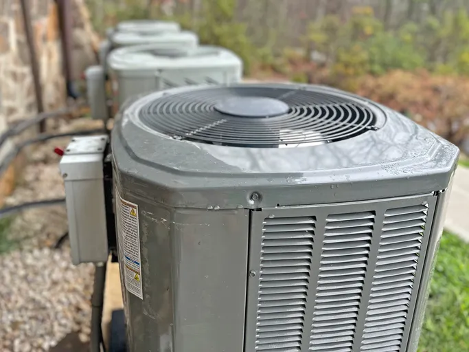 A row of several outdoor air conditioner units lined up outside a building.