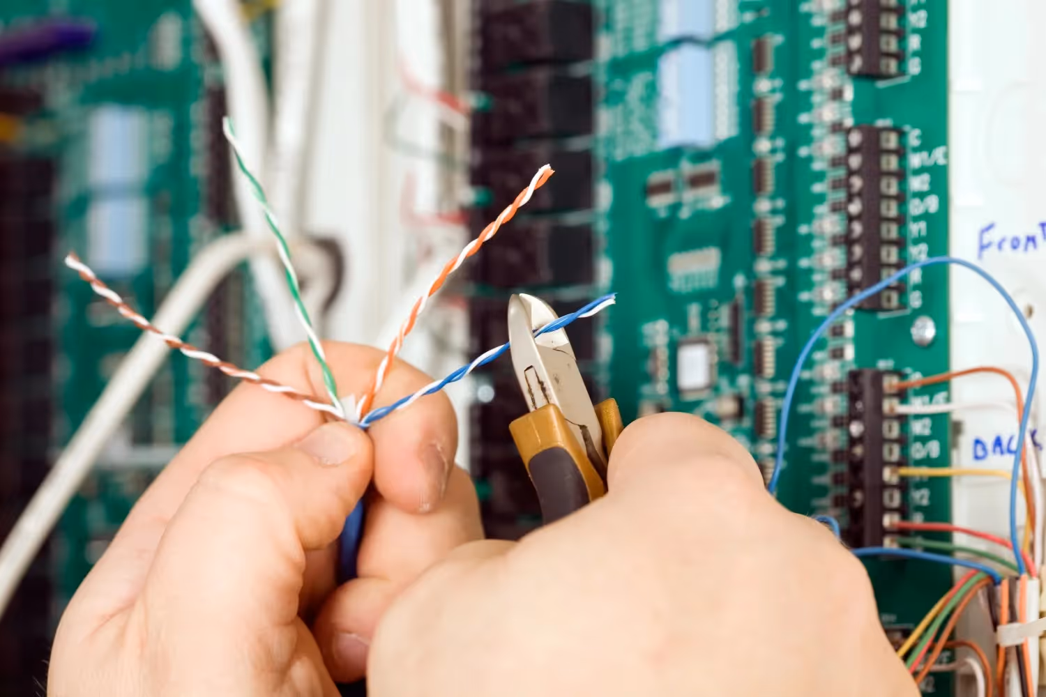 Extreme close-up of hands using wire cutters to trim colorful twisted-pair data cables near a board