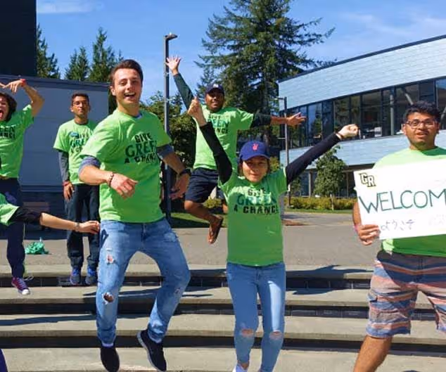 Group of young people wearing green 'Get Green 4 Change' shirts, jumping and smiling outdoors near steps and a building.