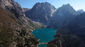 Turquoise mountain lake surrounded by steep rocky peaks and forested slopes under a clear sky.