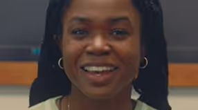 Smiling woman with long braided hair and hoop earrings.