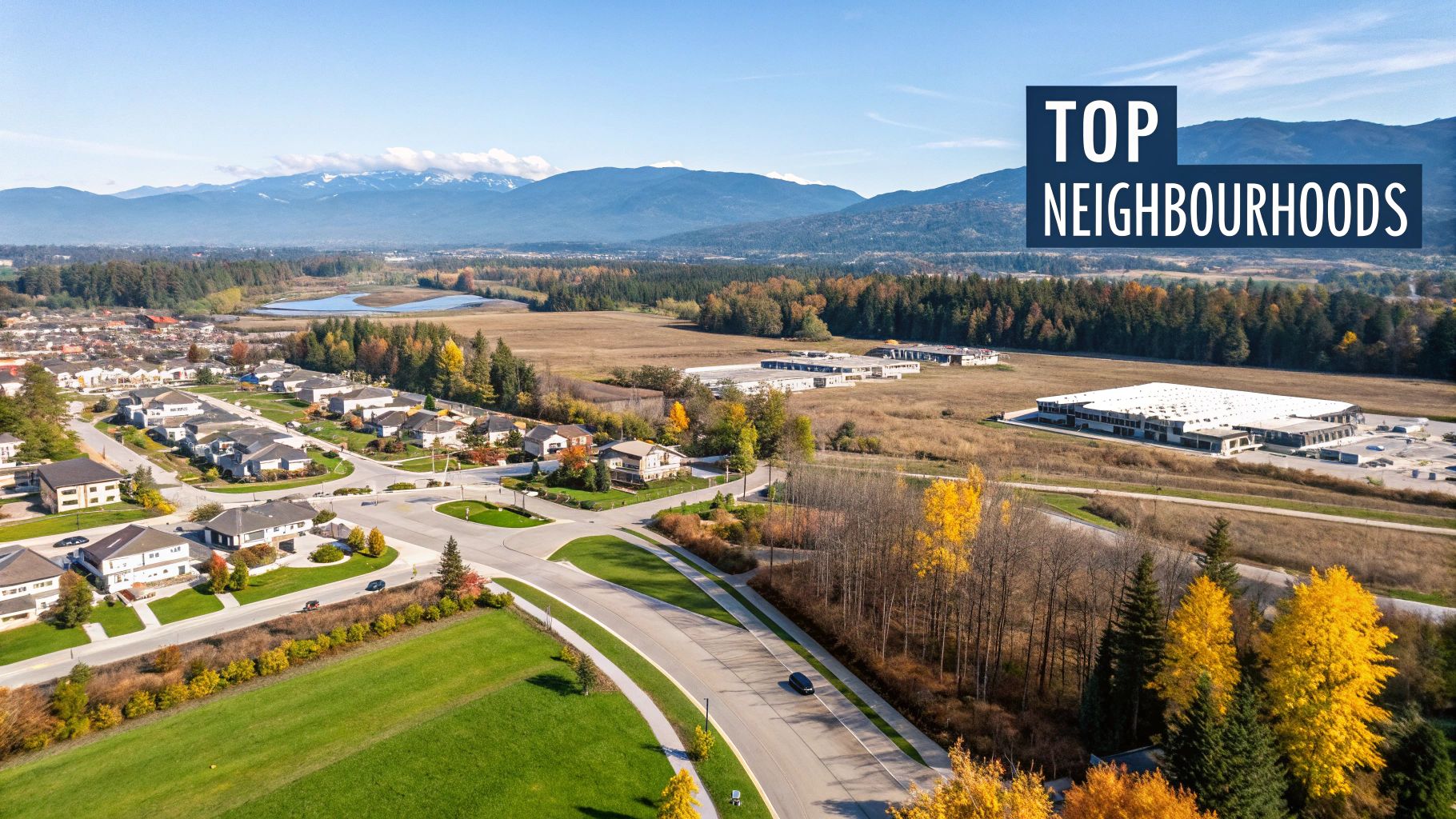Aerial view of a suburban neighborhood with houses, streets, autumn trees, and distant mountains under a blue sky.