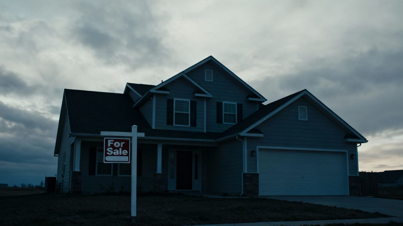House with 'For Sale' sign, cloudy sky.