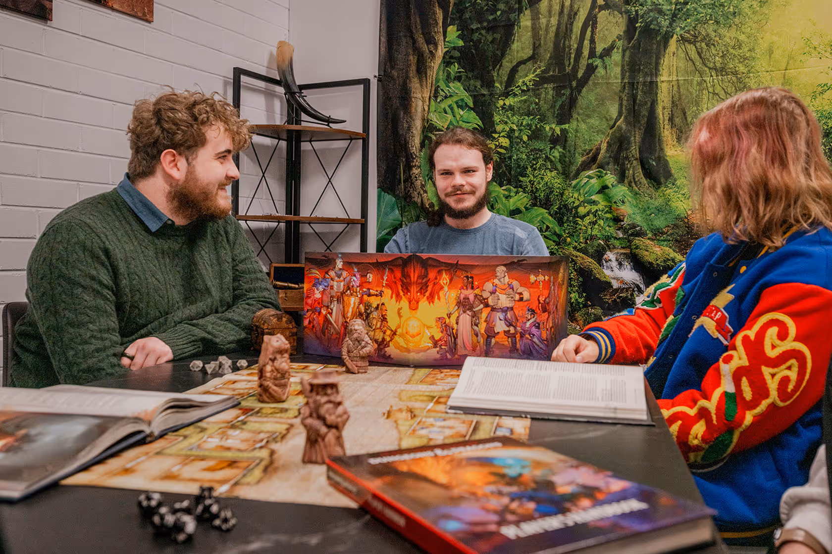 Three people playing a tabletop role-playing game with miniatures, dice, and rulebooks on the table.