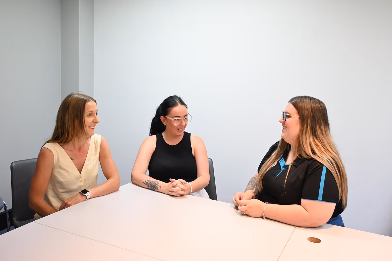 Three women sitting at a table in discussion, smiling and engaged with each other.