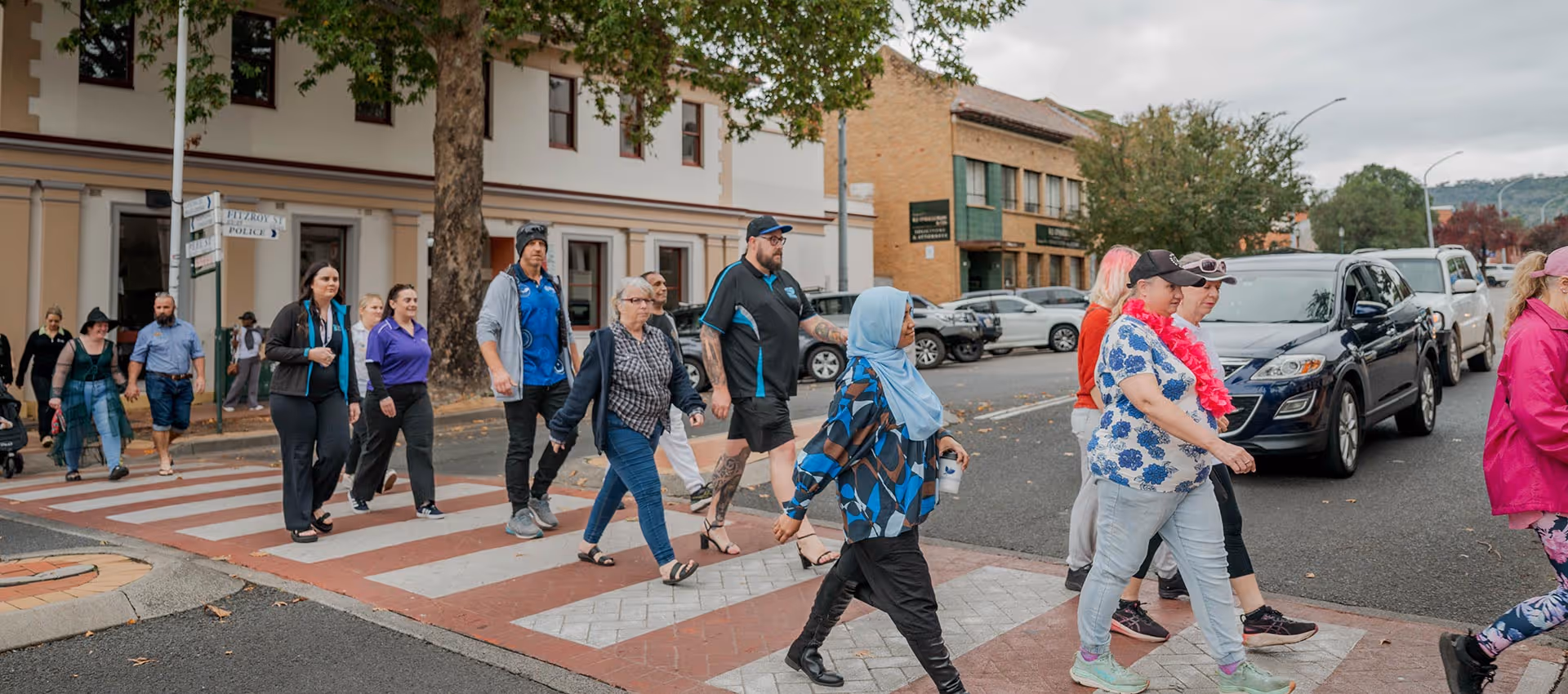 Group of diverse people walking across a crosswalk on a city street during an organized event.