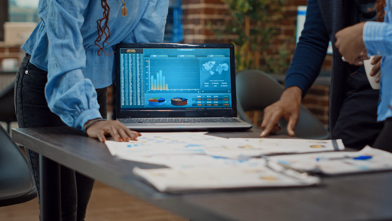 Team reviewing printed reports around a laptop showing analytics dashboards