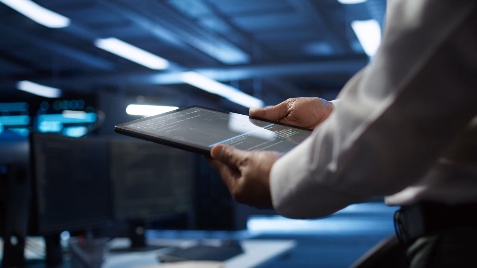 Close-up of a hand holding a tablet in a dimly lit control room