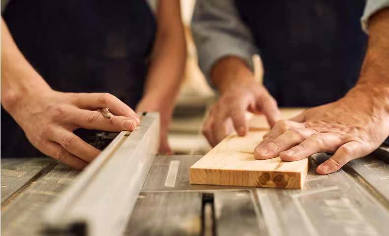 Hands measuring and working with wood on a workshop table