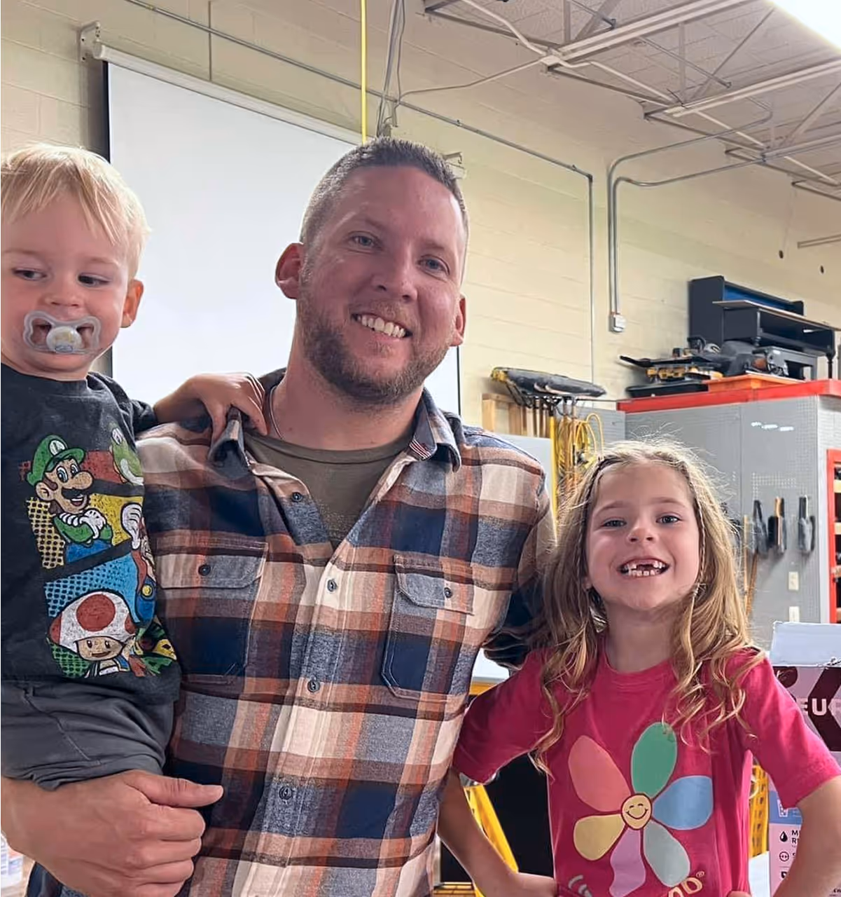 Smiling parent with two children in colorful shirts in workshop setting