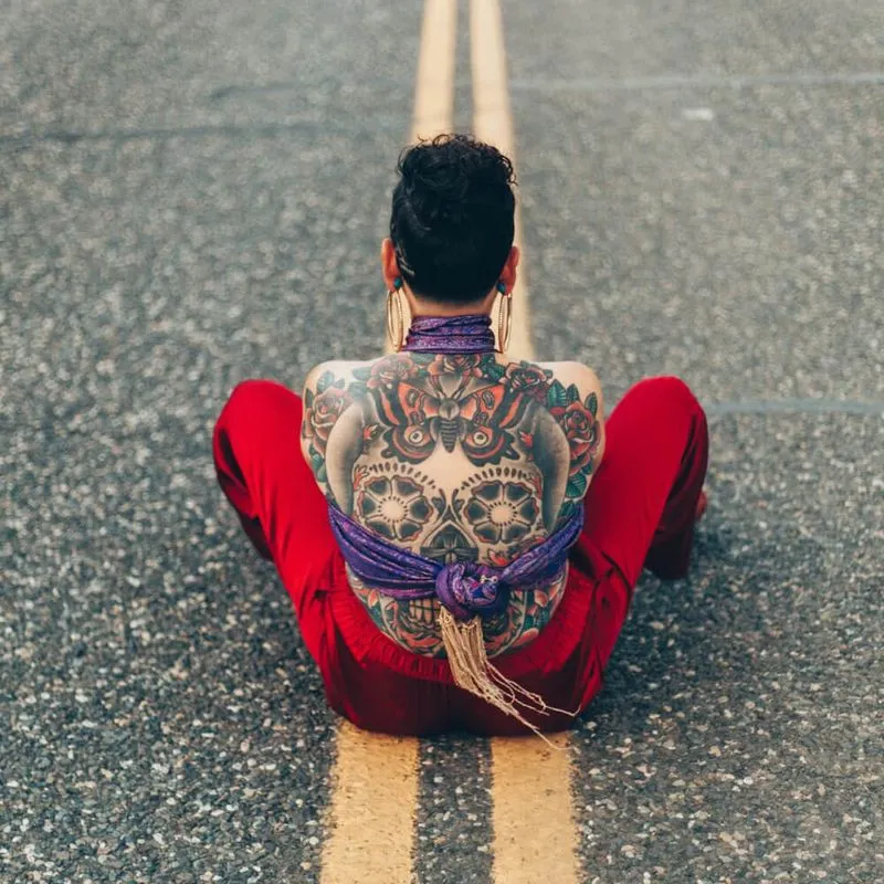 person with calavera tattoo on back sitting in middle of street