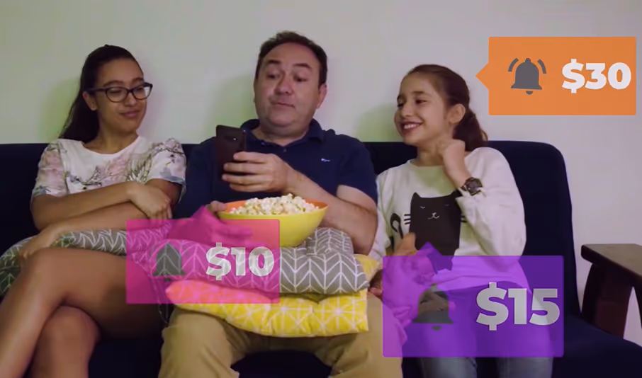 A man sitting on a couch with a bowl of popcorn and a smartphone, flanked by two smiling girls, with colorful price tags showing $10, $15, and $30.