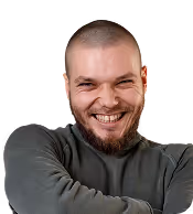 Smiling man with shaved head and beard wearing dark long-sleeve shirt, arms crossed.