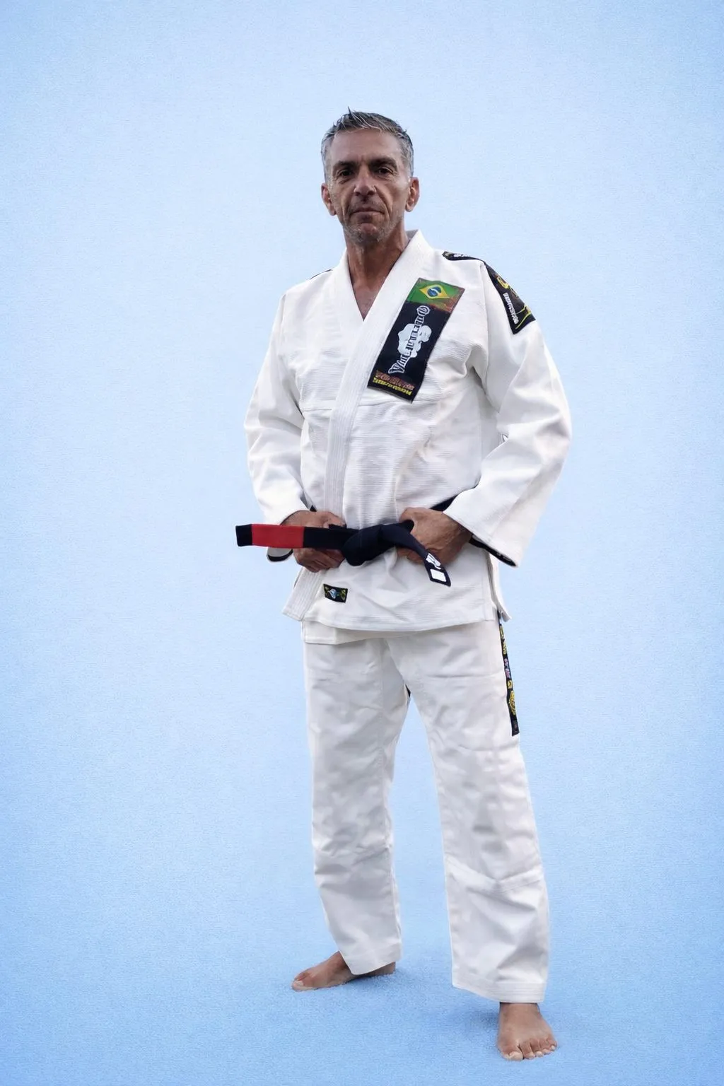 Christian Sardella, professeur de jiu-jitsu brésilien à Strasbourg, ceinture noire, en kimono blanc sur fond bleu clair.