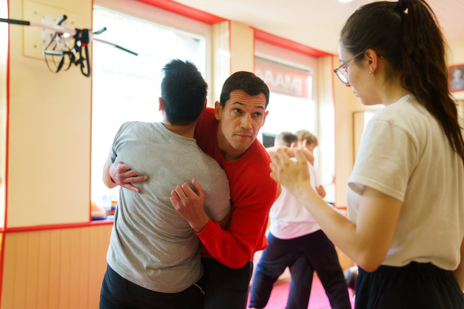 Mateo en sweat rouge démontrant une technique de clé articulaire lors d’un cours de self défense avec plusieurs élèves observant.