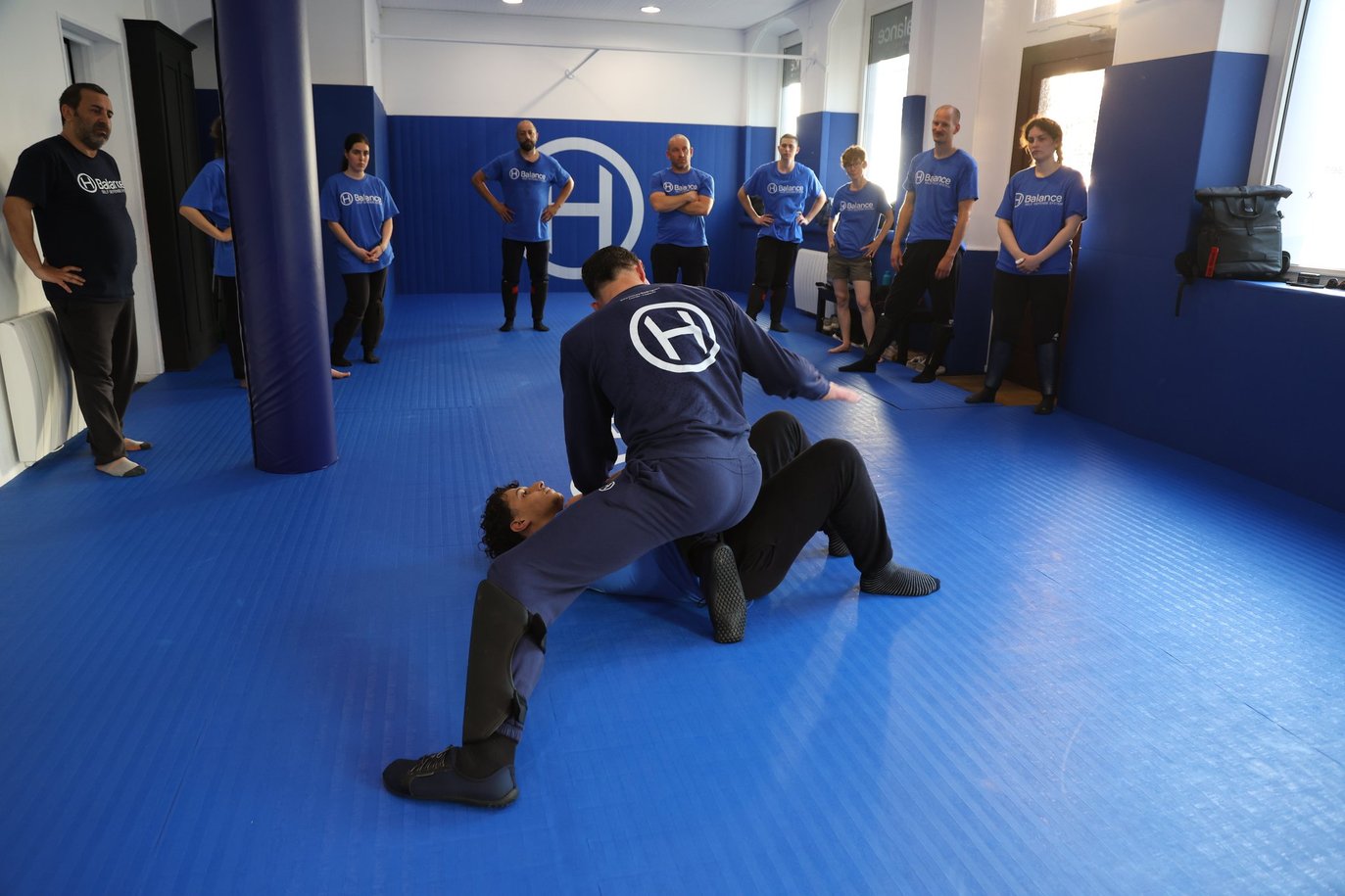 Cours de self-défense à H Balance Studio à Strasbourg : travail de défense et de contrôle au sol sous le regard du groupe.