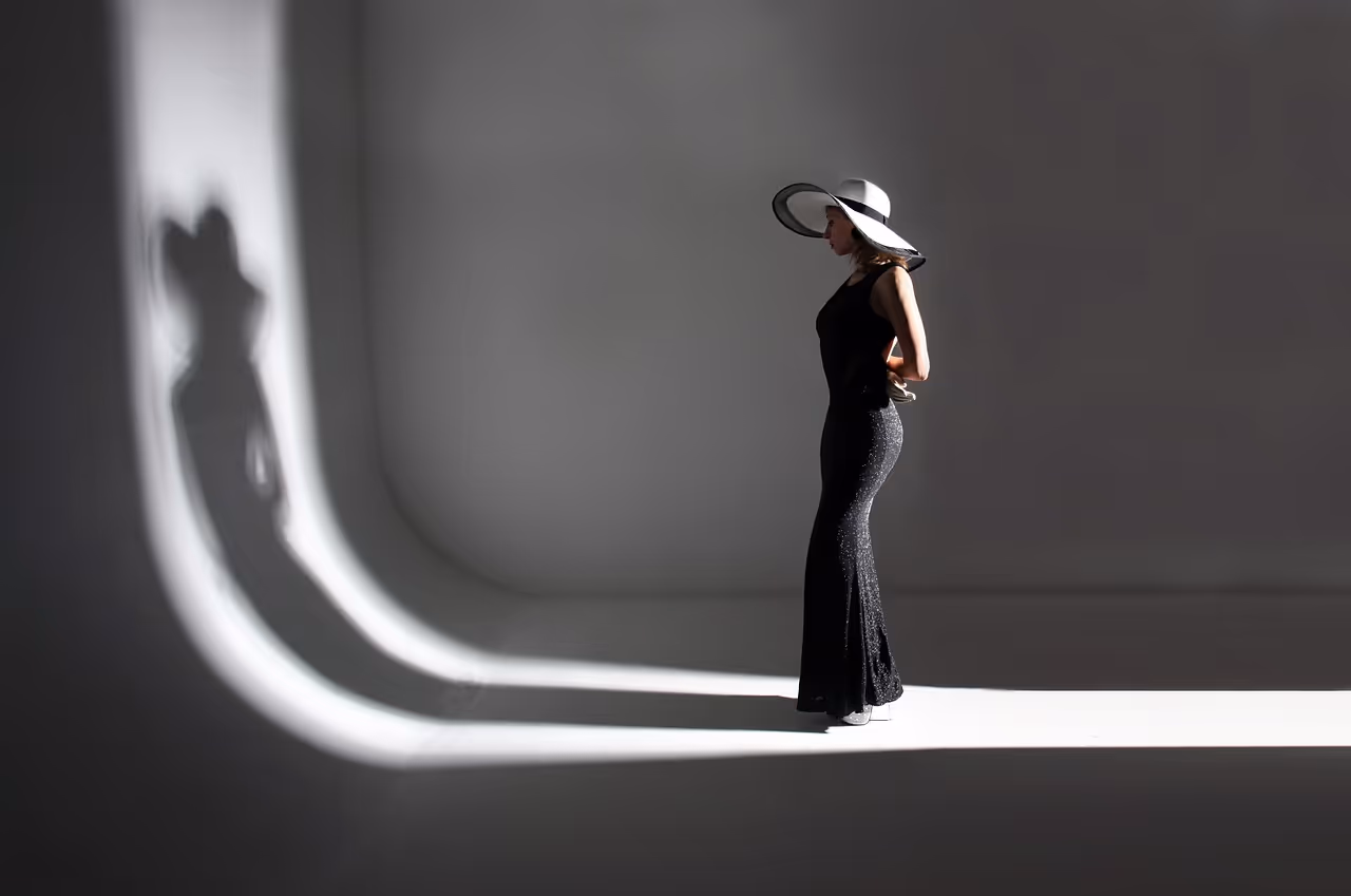 a woman wearing hat looking at her shadow in a dark room