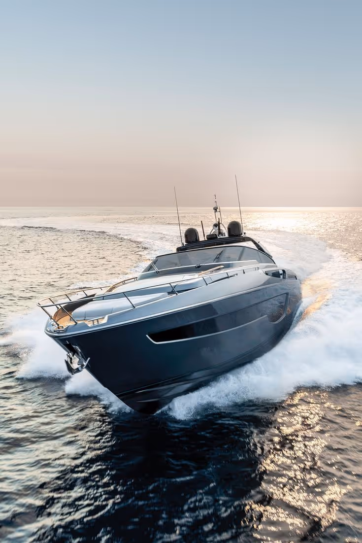 Luxury yacht speeding on calm ocean water with a clear sky at sunset.