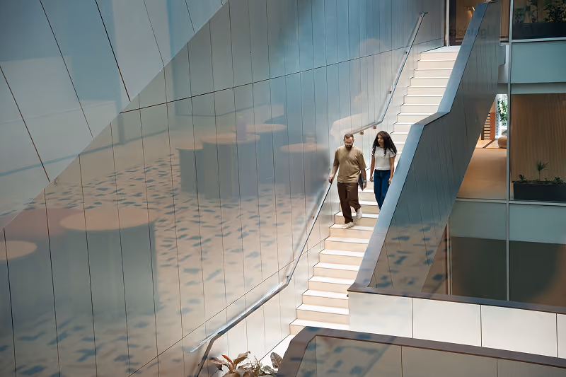 Man and woman walking down stairs inside a modern building with reflective walls.