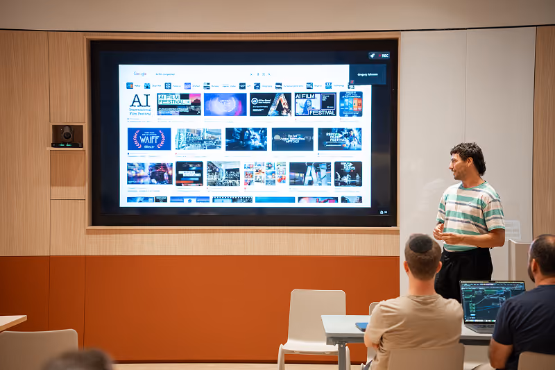 Man in striped shirt presenting AI film festival images on a large screen to seated audience.