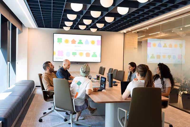 Five people seated around a conference table in a modern office with a presentation on a screen.