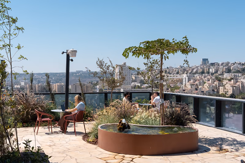 People sitting at tables in a rooftop garden with plants and a small round water feature.