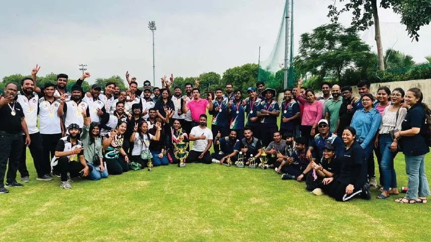 Large group of men and women posing outdoors on grass, some wearing medals and holding trophies, celebrating a sports achievement.