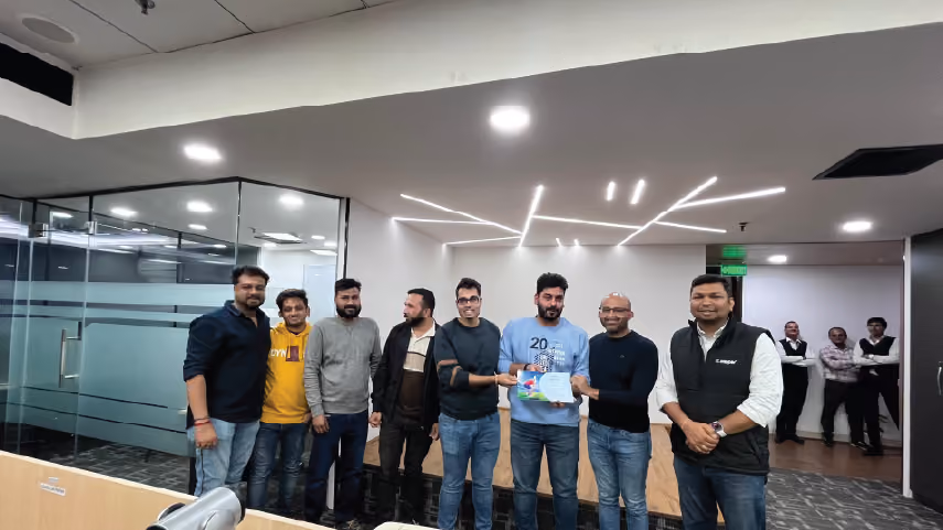 Group of eight men standing in an office, two men in the center holding a certificate and smiling.
