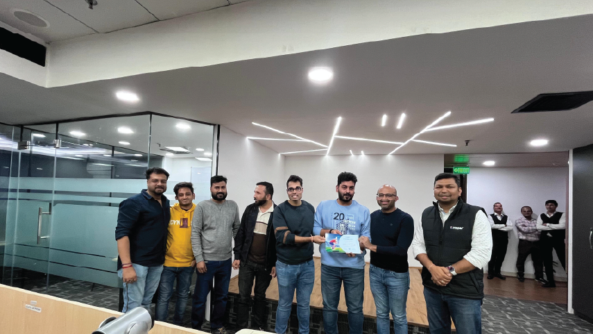 Group of eight men standing in an office, two men in the center holding a certificate and smiling.