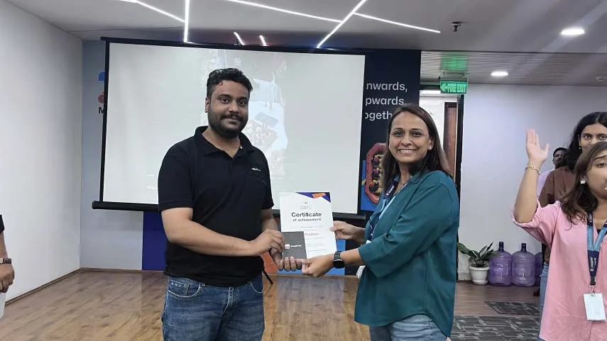 A man and a woman smiling while holding a certificate of achievement together in an office setting.