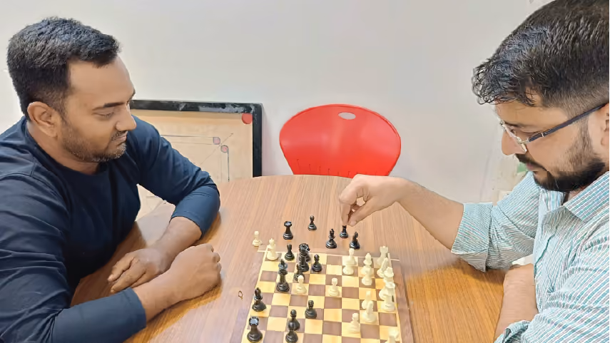 Two men sitting across from each other at a wooden table, playing a game of chess.
