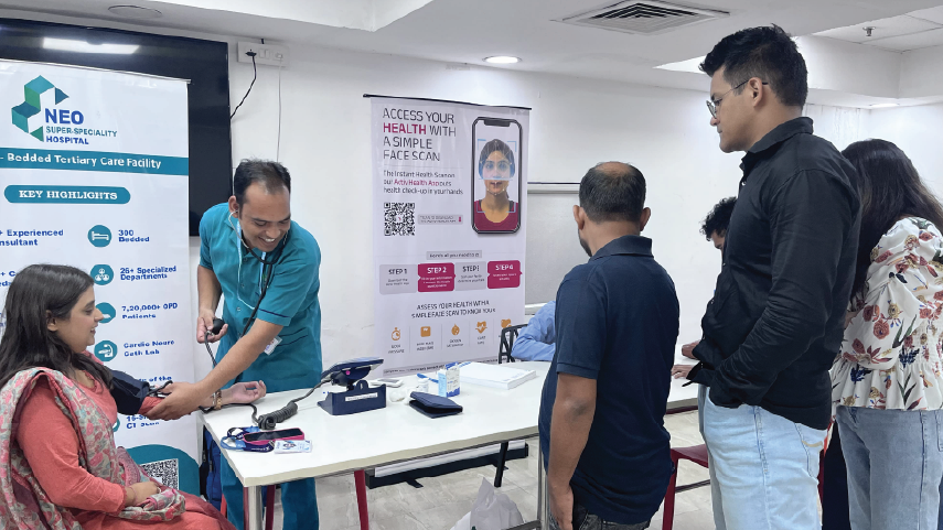 Healthcare professional in teal scrubs taking blood pressure of seated woman while three people wait in line.