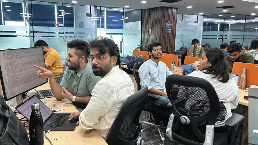 Group of professionals collaborating and working on laptops in a modern office with glass walls.